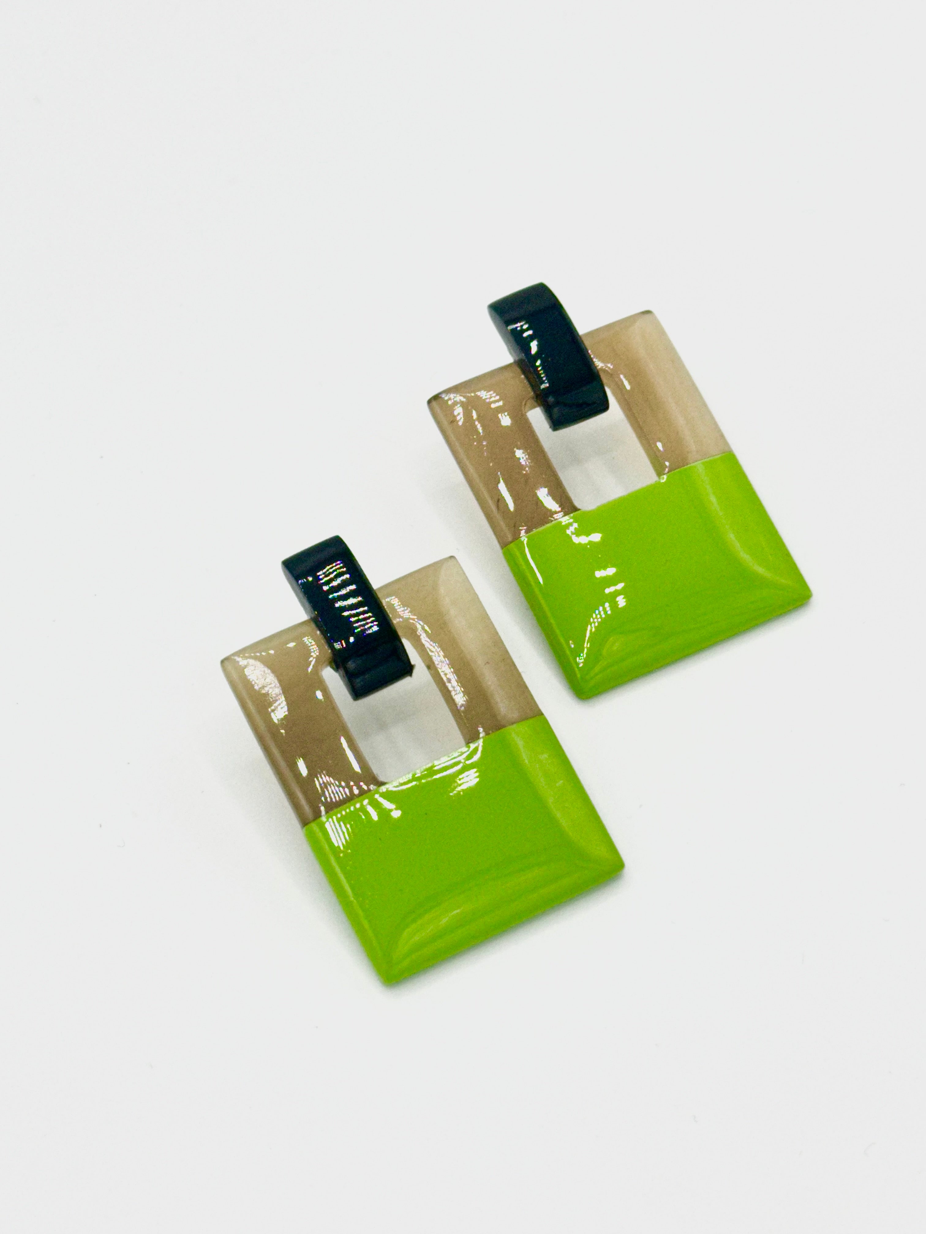 Two green square earrings with black and white accents on a light gray background
