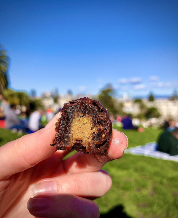 Hand holding a chocolate truffle with a park in the background