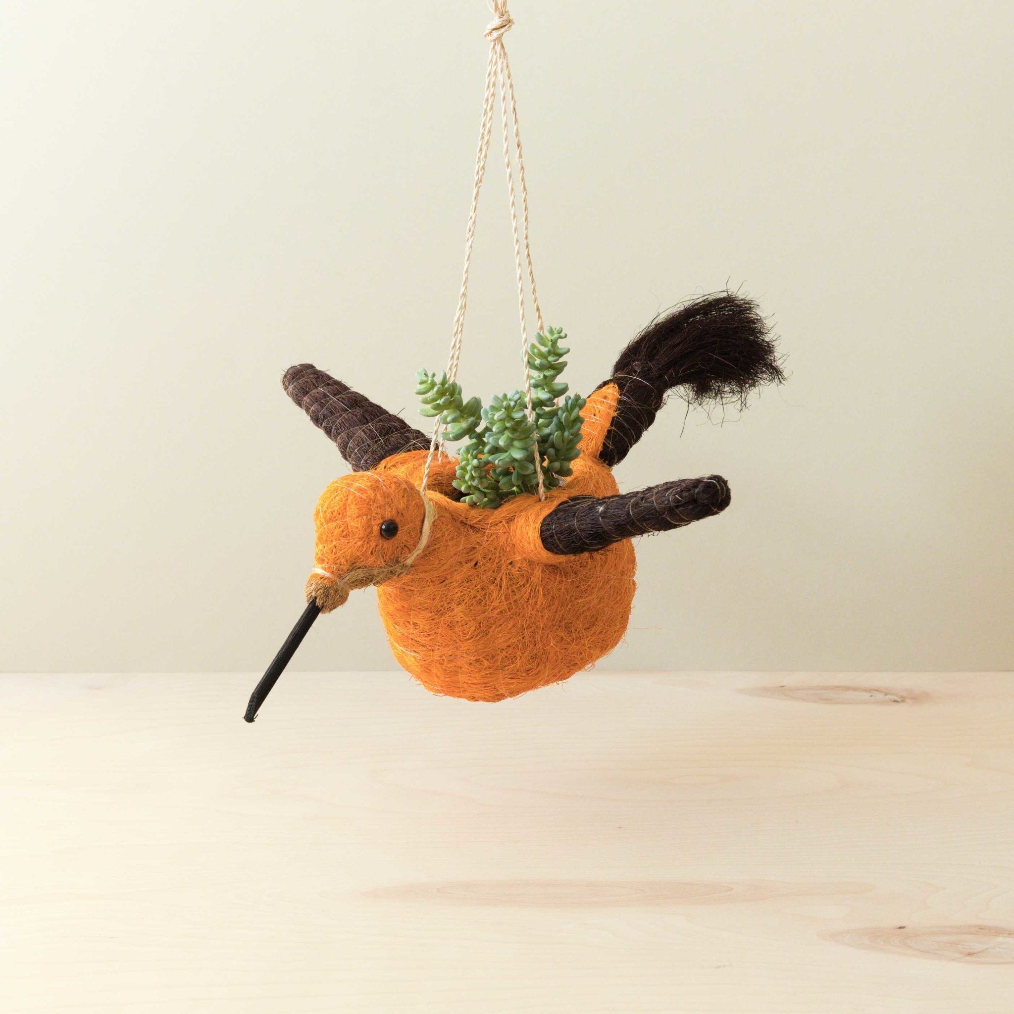 Hanging planter shaped like a bird with a small plant inside on a light background