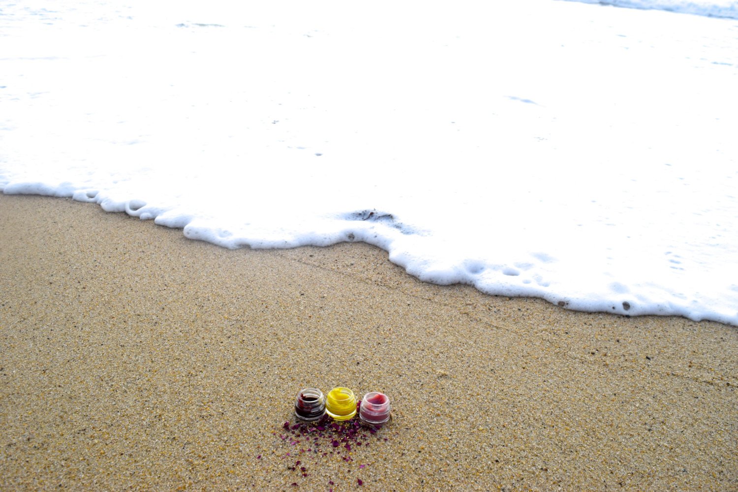 Three small colorful objects on a sandy beach with waves in the background