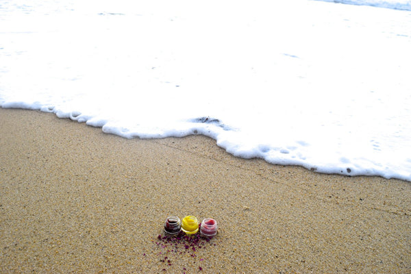 Three small colorful objects on a sandy beach with waves in the background
