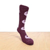 Maroon sock with dog pattern on a wooden floor. Discover our fun Pronk & Play Alpaca Socks, featuring a cheerful design for adults and kids. Made with a soft alpaca blend, these USA-designed socks are comfortable and durable. Shop now and add a little joy to your step.