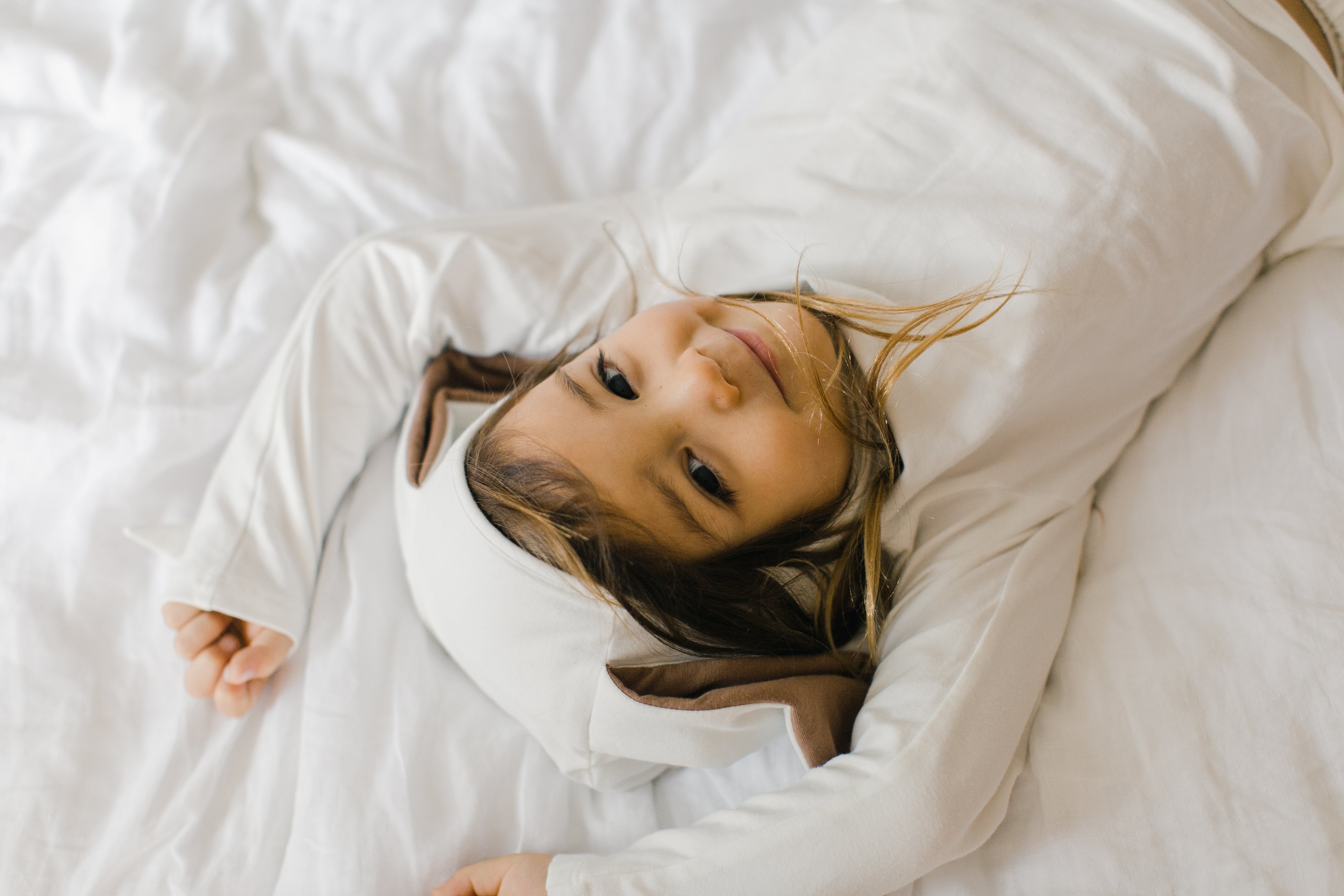 Child lying on a white bedspread with a pillow