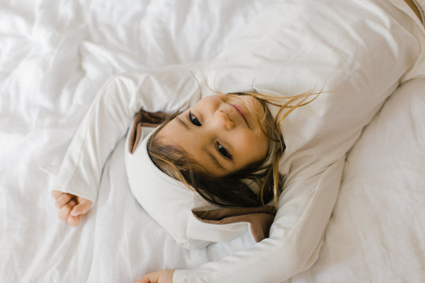 Child lying on a white bedspread with a pillow