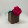 Crocheted red rose on a wooden block against a white background