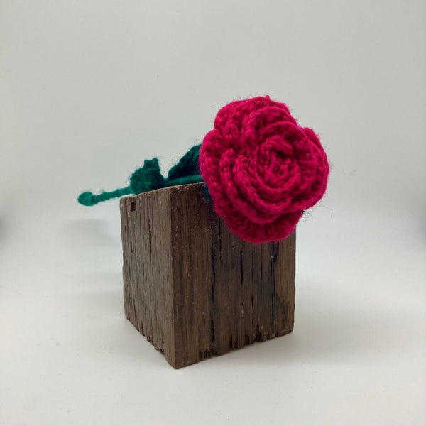 Crocheted red rose on a wooden block against a white background