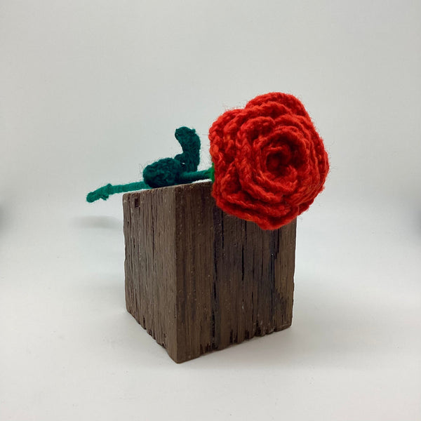 Red crocheted rose on a wooden block against a white background