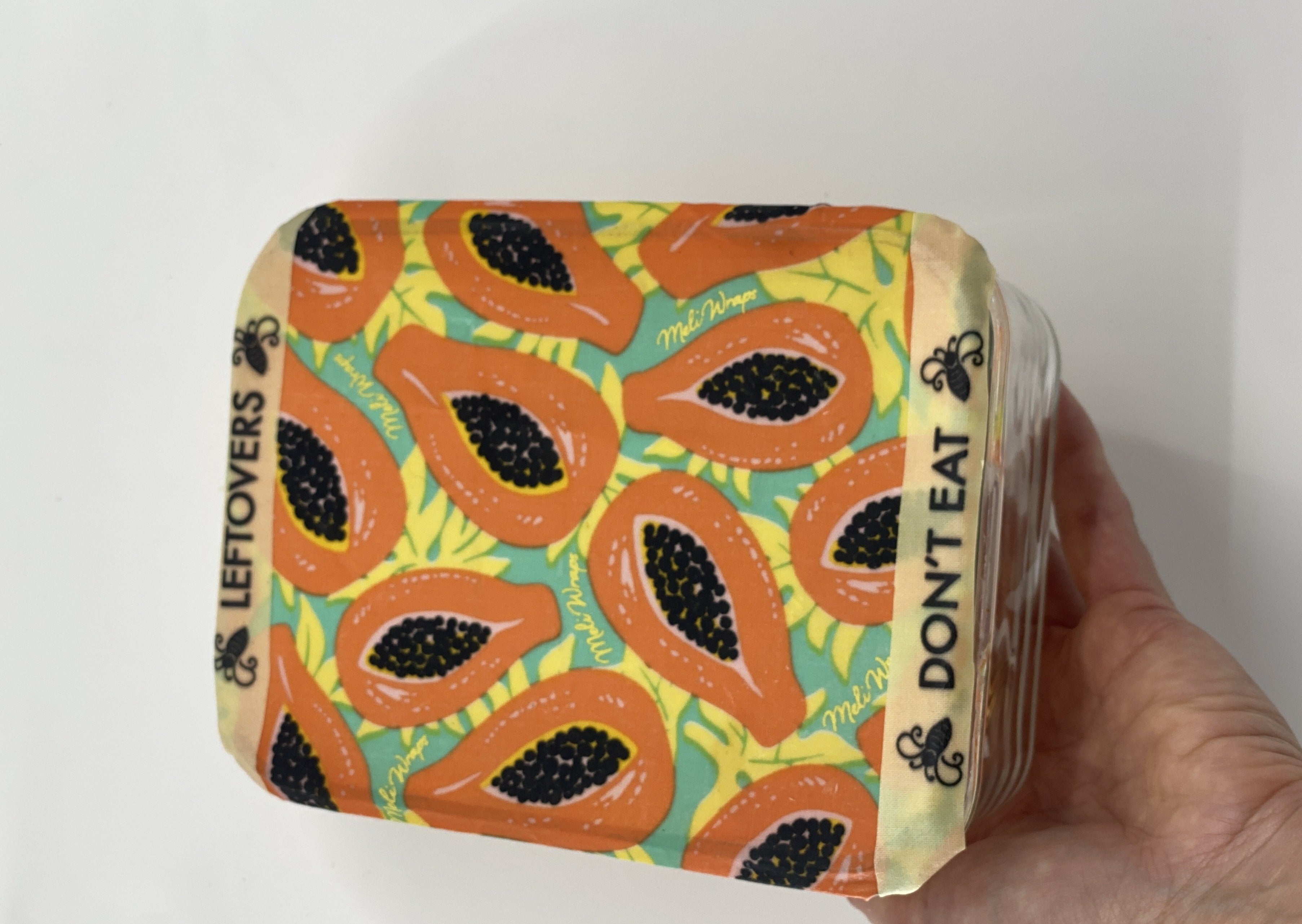 Container with papaya pattern and 'Don't Eat' label held by a hand on a white background