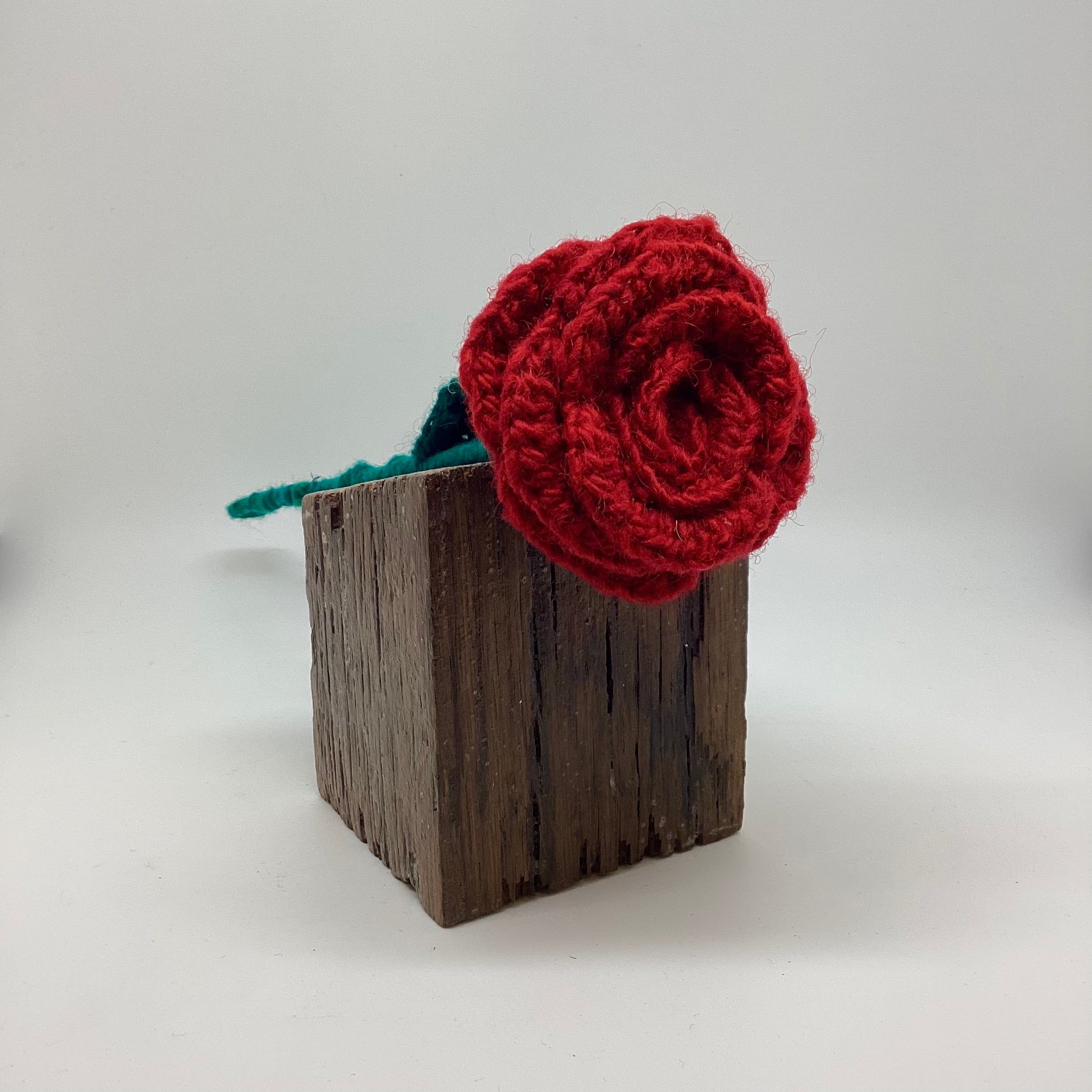 Red knitted flower on a wooden block against a light gray background