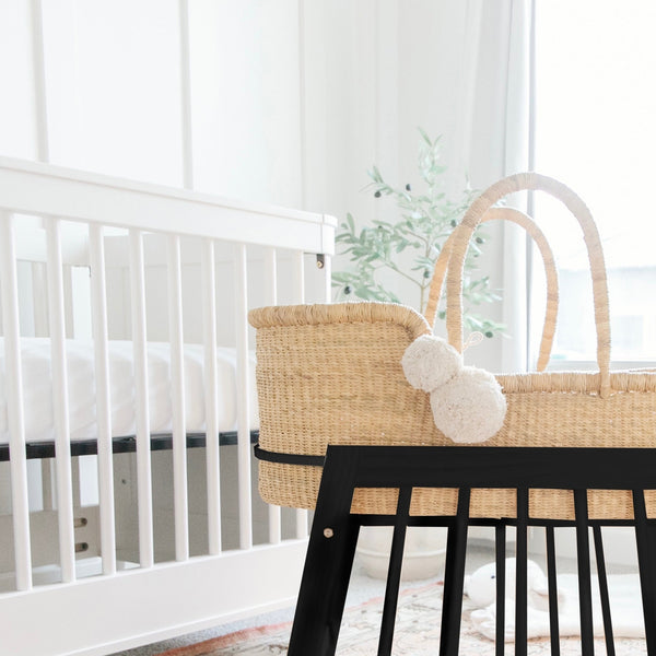 Nursery with a white crib and a wicker Moses basket with black base.