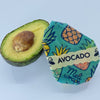 Avocado cut in half with a reusable avocado wrap on a light blue background