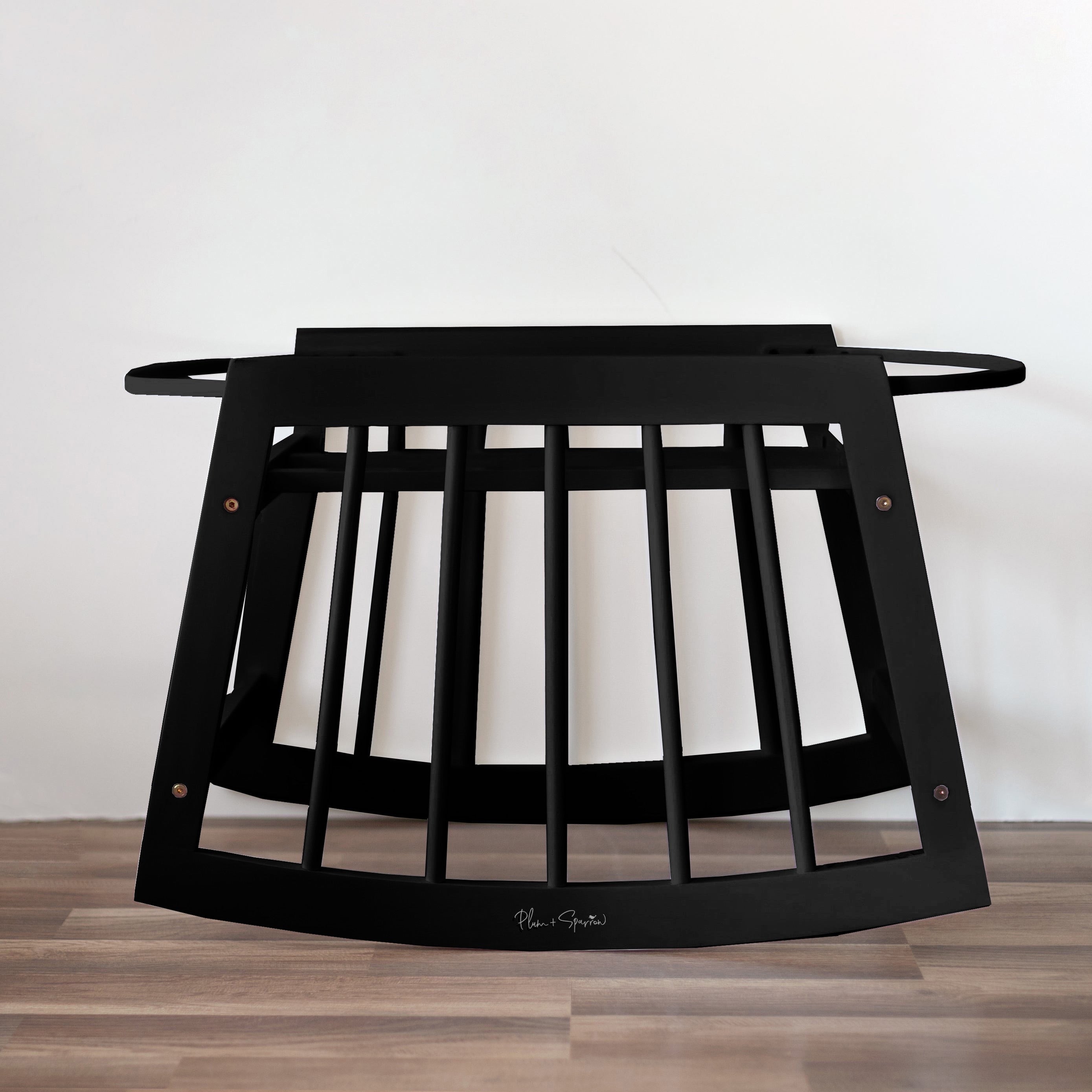 Black metal baby crib on a wooden floor with a white wall background