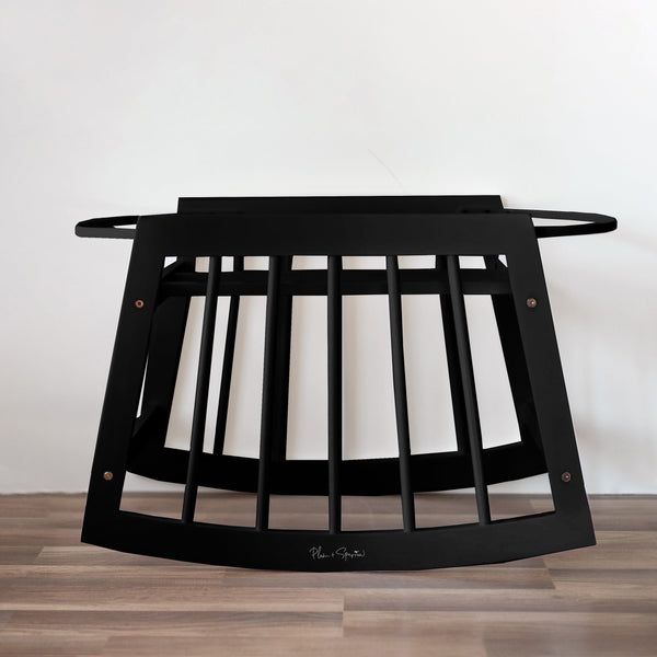 Black metal baby crib on a wooden floor with a white wall background