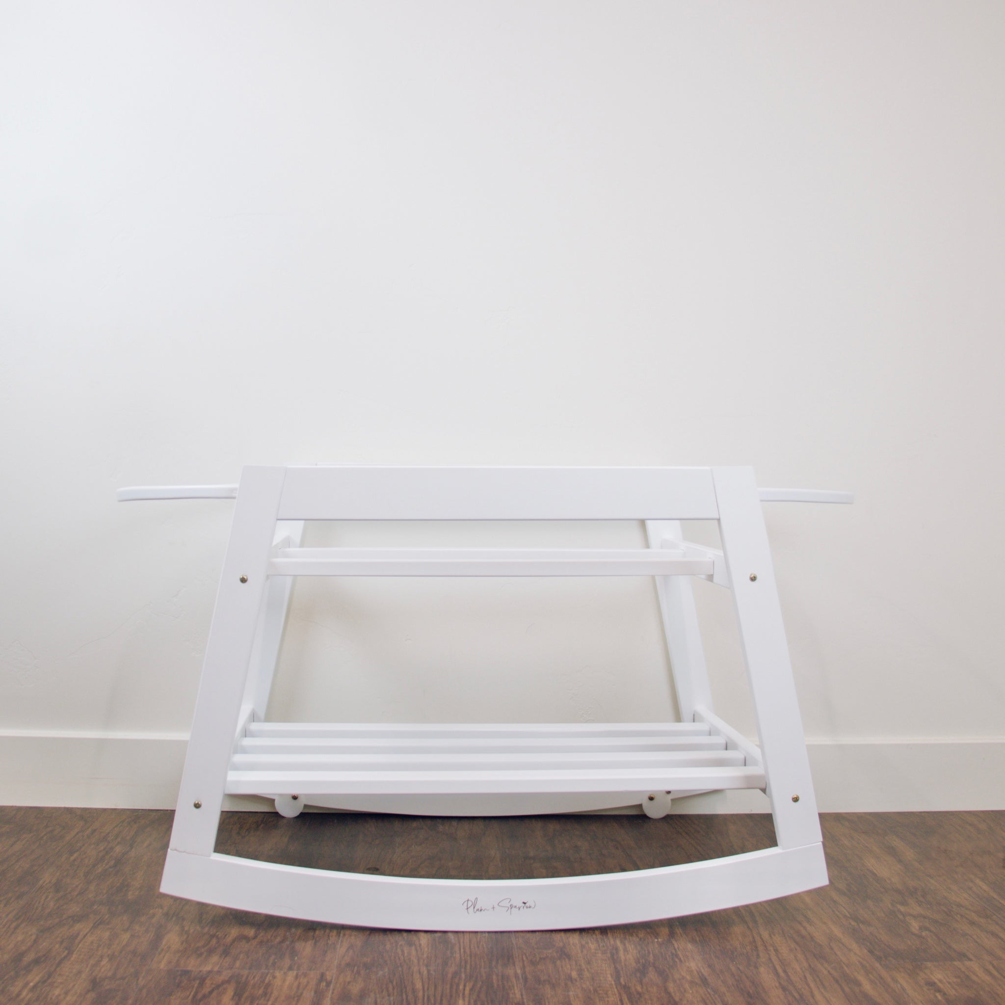 Close-up detail of the Plum+Sparrow rocking bassinet stand brake mechanism and adjustable straps in white