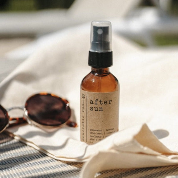 Brown spray bottle labeled 'after sun' with sunglasses on a towel