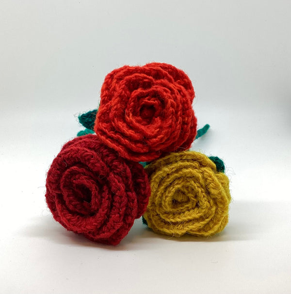 Three crocheted roses in red, yellow, and green on a white background