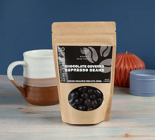 Package of chocolate-covered espresso beans with a mug and candle in the background
