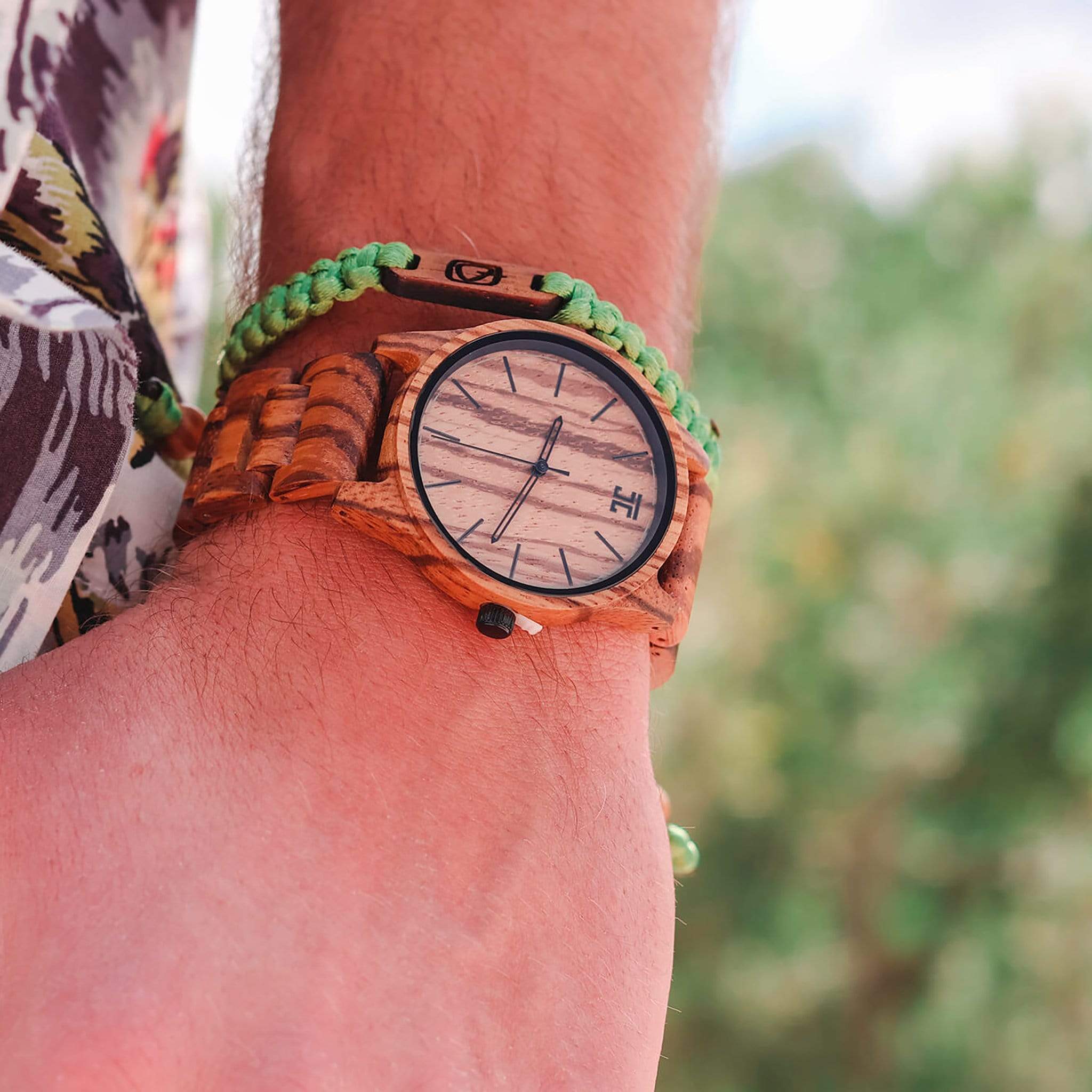 Wooden wristwatch on a person's wrist with a blurred natural background