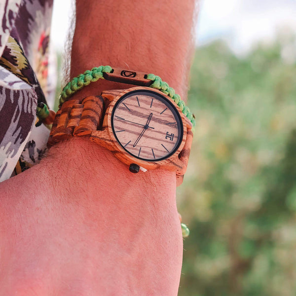 Wooden wristwatch on a person's wrist with a blurred natural background