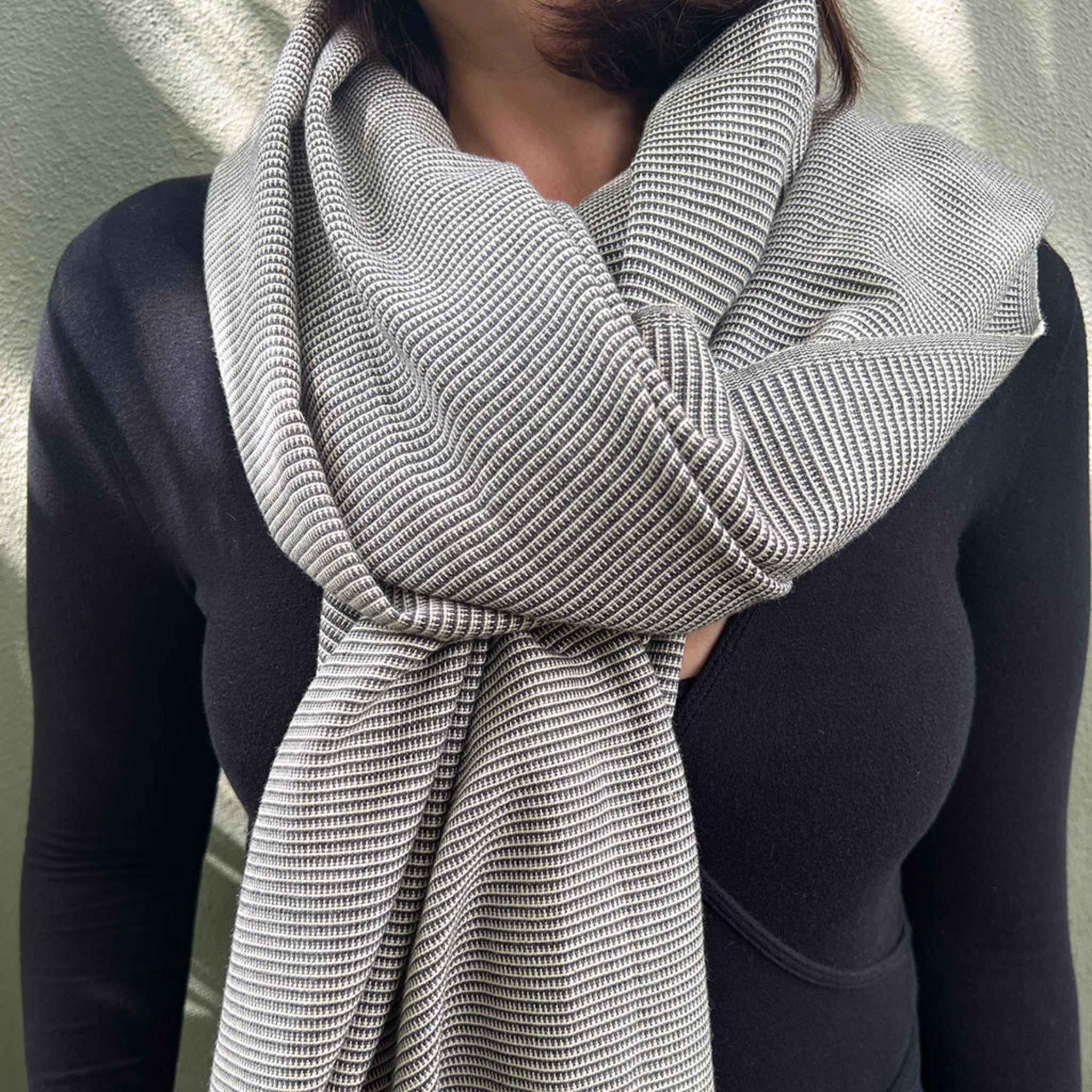 Person wearing a knitted gray cotton scarf against a neutral background