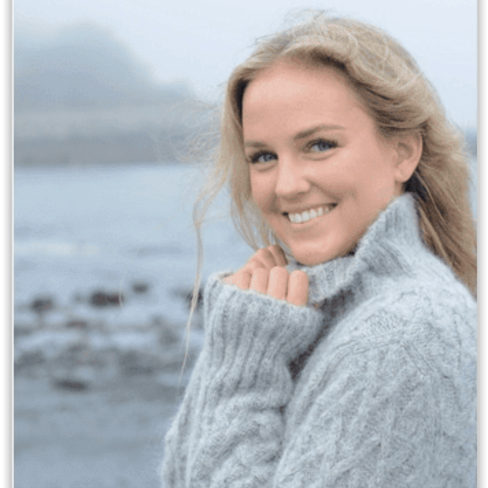 Woman wearing a gray sweater with a stack of similar sweaters below on a wooden surface.