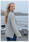 Woman wearing a gray knitted sweater by a body of water