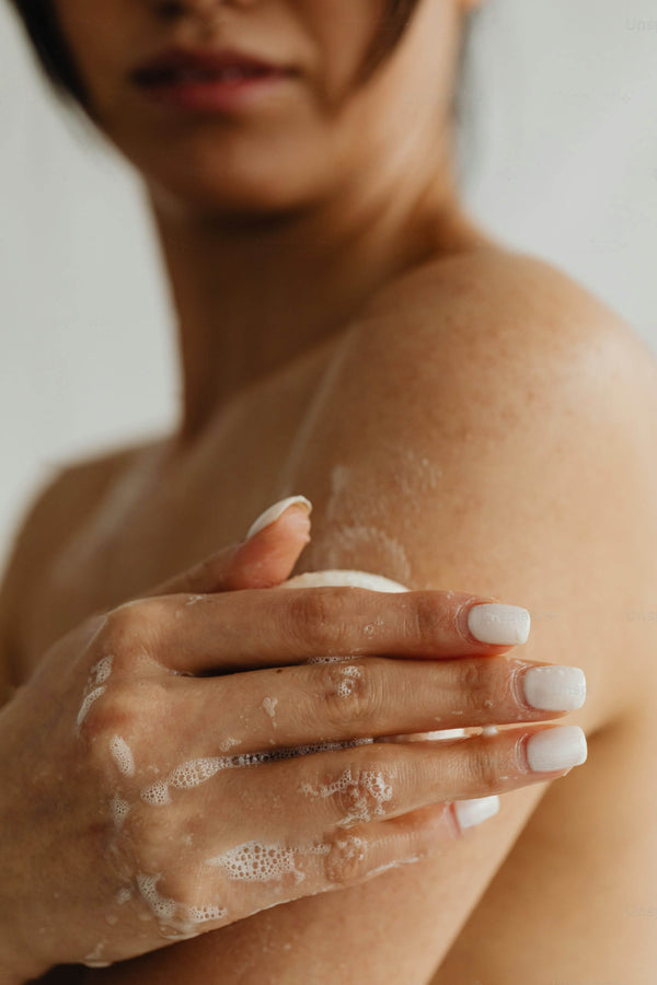 Person applying a white cream or lotion to their shoulder with a blurred background