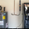 Water heater and refrigerator against a white wall with visible pipes.