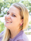 Close-up of magenta and brass rhombus earrings showing enamel detail and geometric shape by Fair Anita