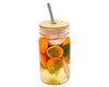 Glass jar with a wooden lid and metal straw, filled with orange slices and leaves on a white background