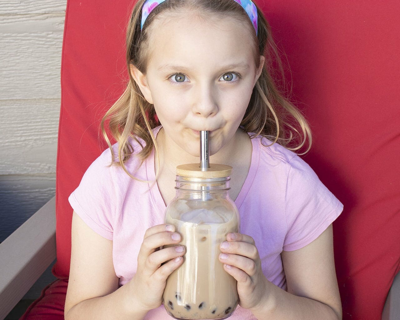 Young girl drinking from a large glass with a straw against a red background