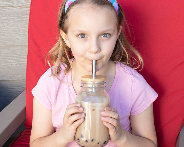 Young girl drinking from a large glass with a straw against a red background