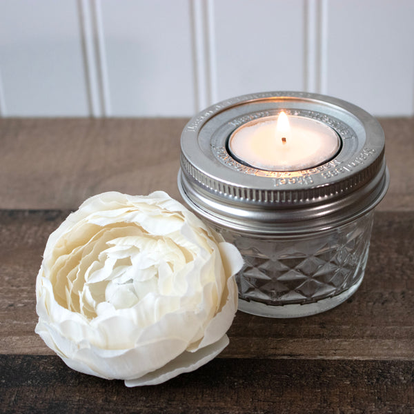 Candle in a decorative jar with a white flower on a wooden surface