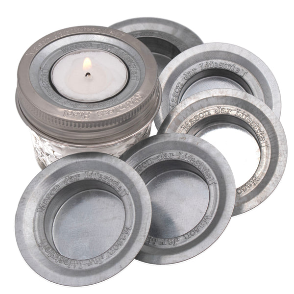 Set of Mason jar lids with a lit candle inside one of them on a white background