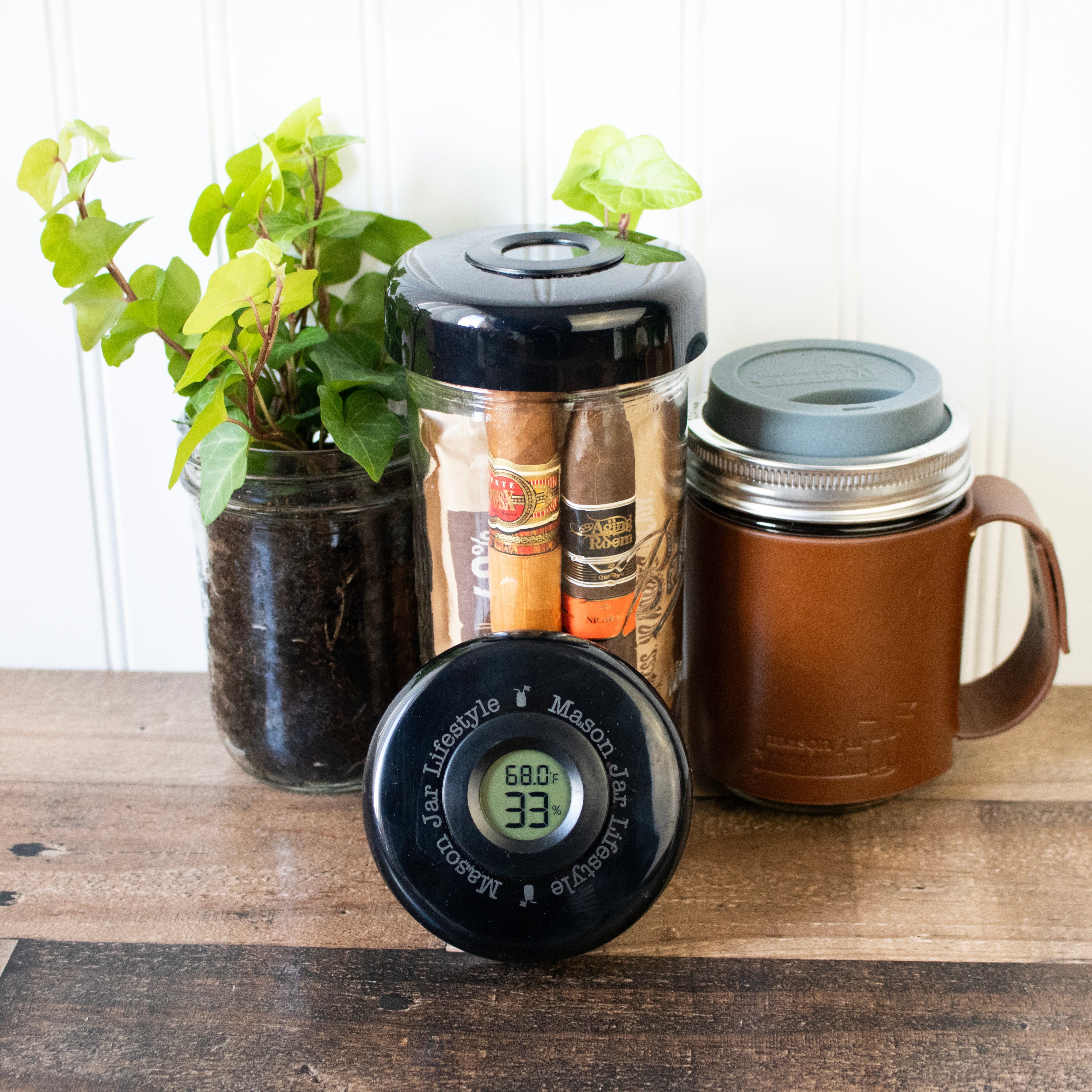 Two mason jar coolers with lids, a digital thermometer, and a potted plant on a wooden surface.