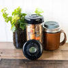 Two mason jar coolers with lids, a digital thermometer, and a potted plant on a wooden surface.