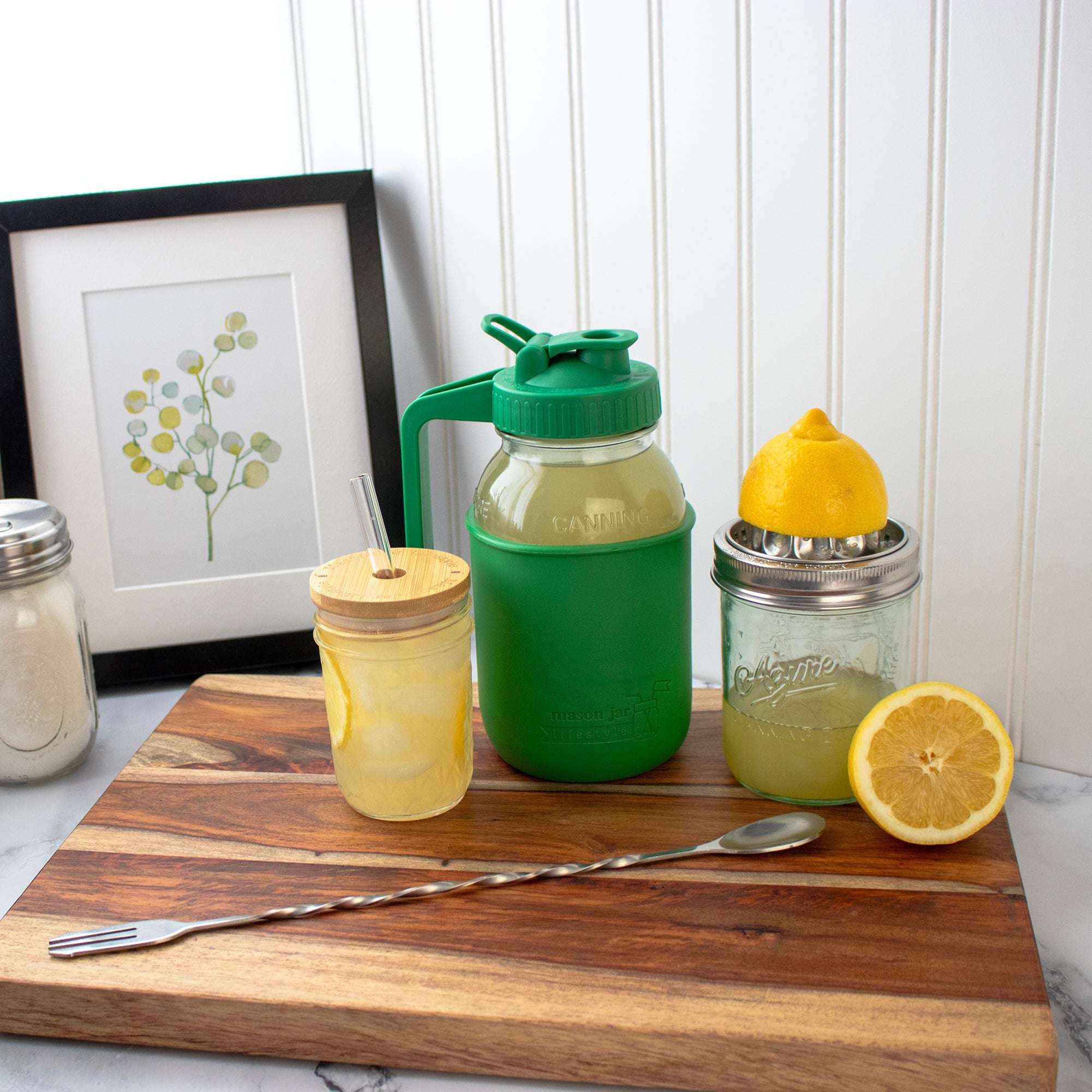 Green and yellow mason jar drinks with lemon slices on a wooden cutting board.