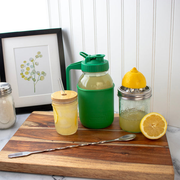 Green and yellow mason jar drinks with lemon slices on a wooden cutting board.