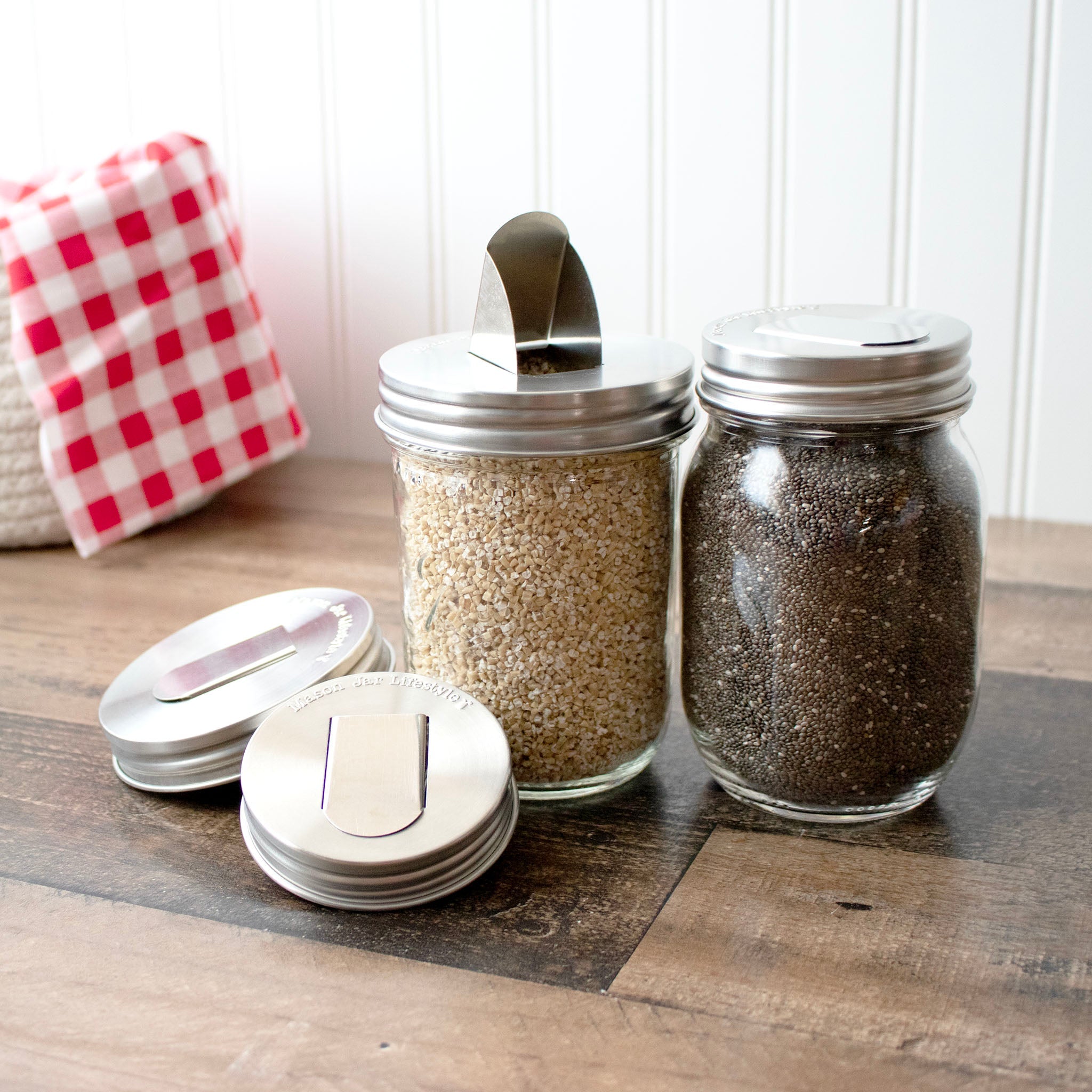 Glass jars with metal lids on a wooden surface with a red and white checkered cloth in the background.