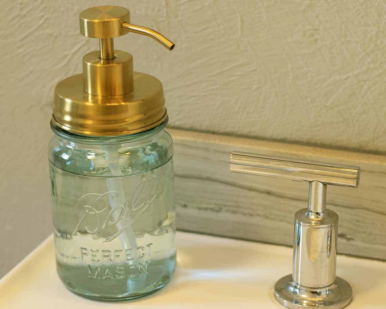 Glass mason jar with gold pump top on a bathroom counter