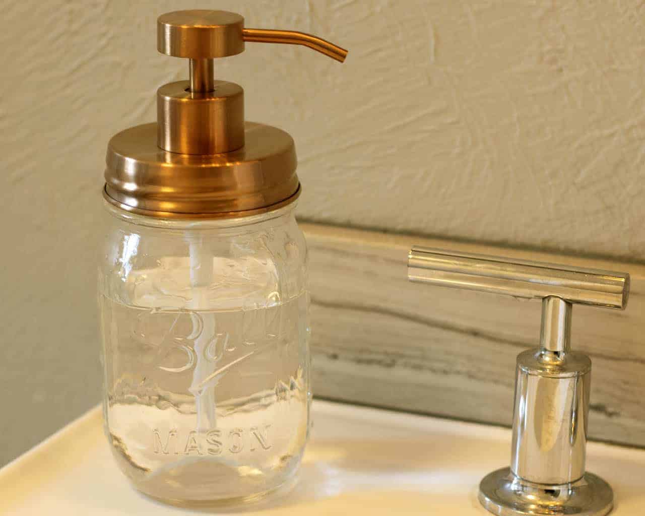 Glass mason jar soap dispenser with gold pump on a bathroom counter.