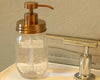 Glass mason jar soap dispenser with gold pump on a bathroom counter.