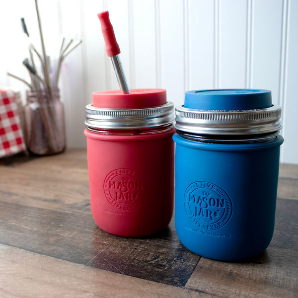 Red and blue mason jar cups with straws on a wooden surface.