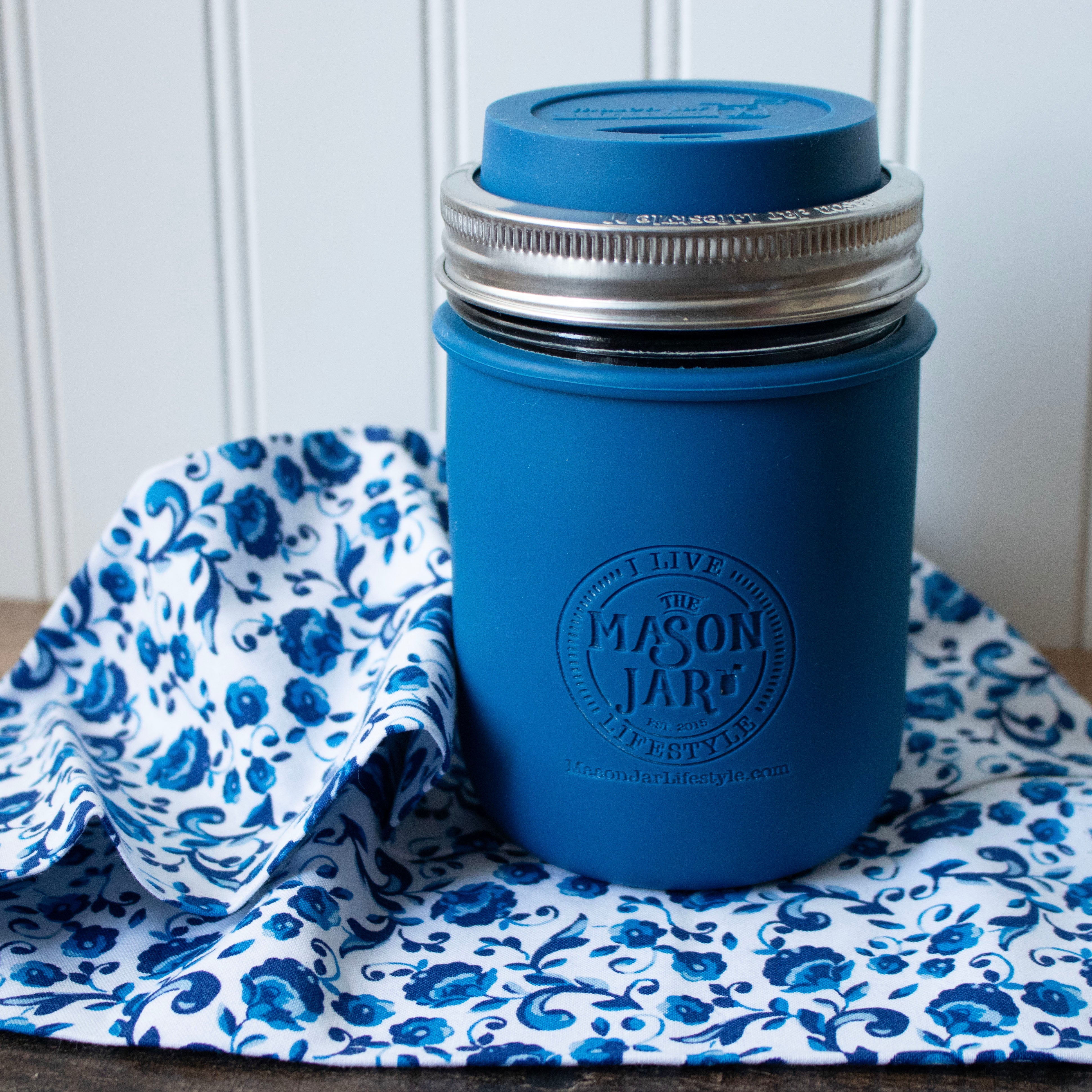 Blue mason jar with a lid on a floral cloth against a white paneled wall.