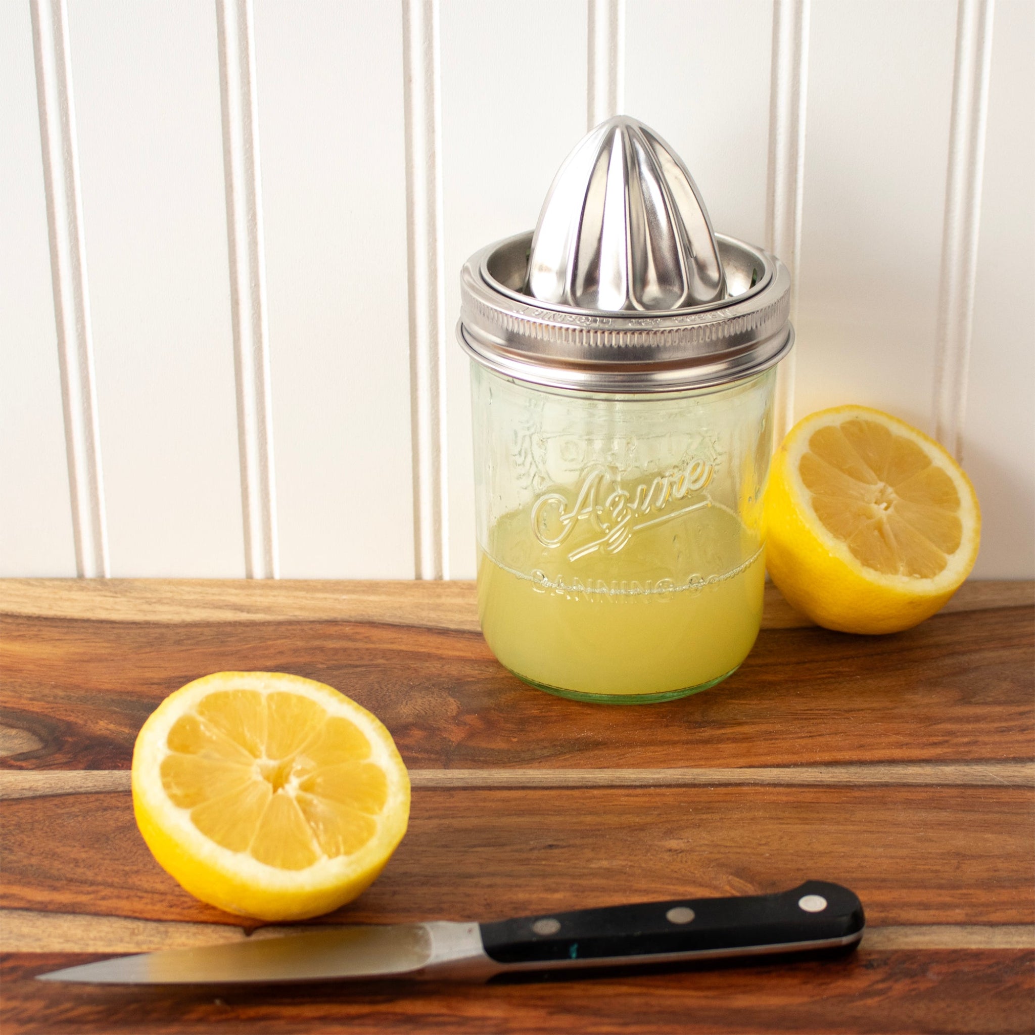 Mason jar with lemon juice and lemon squeezer on a wooden surface