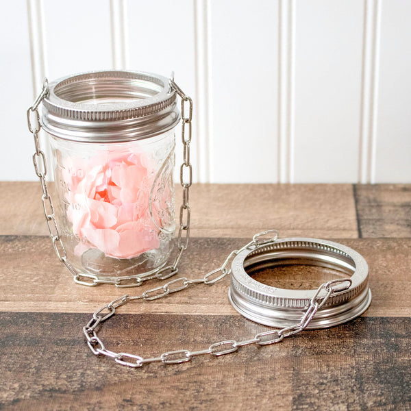 Glass jar with metal chain and pink flower on wooden surface