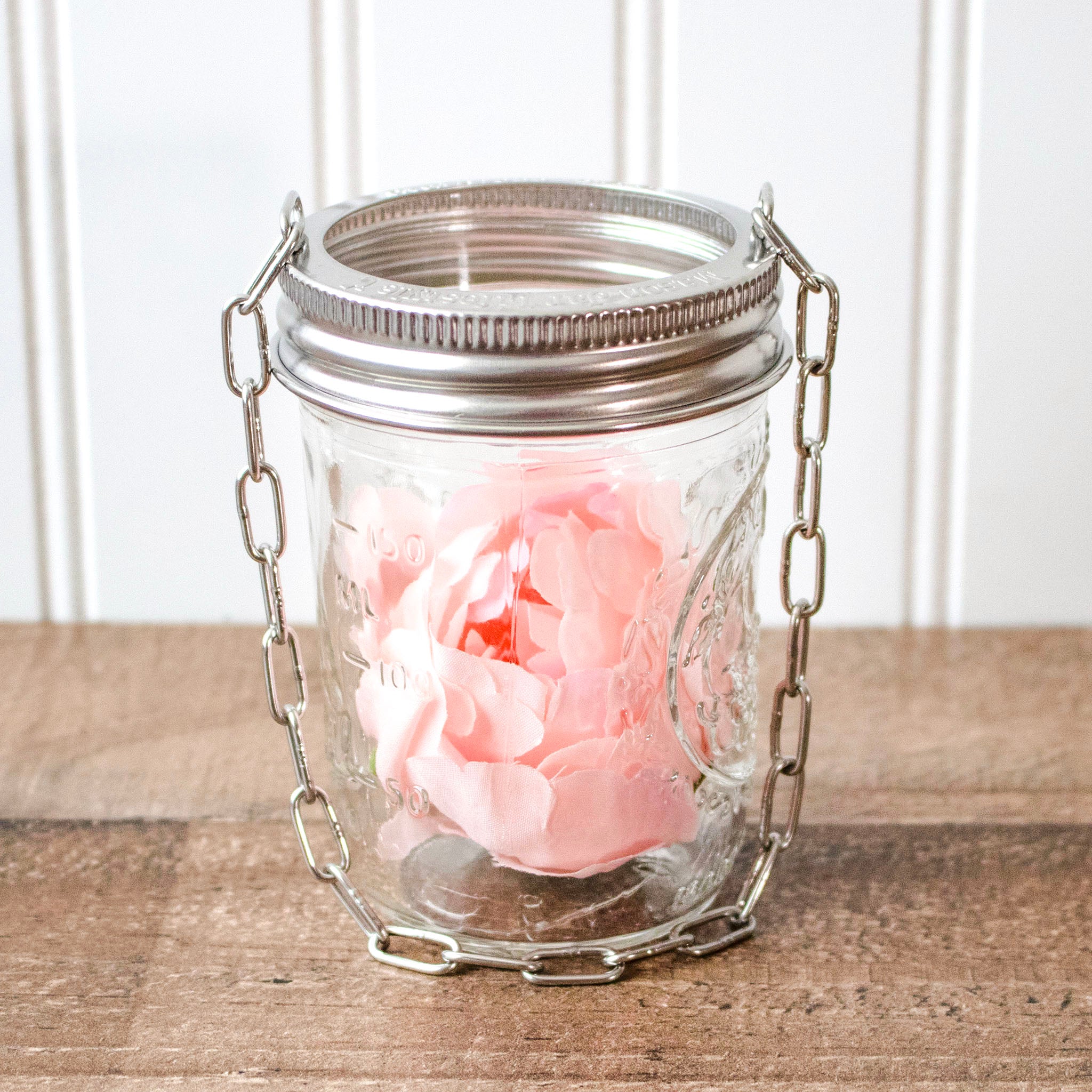 Glass jar with pink flower and metal chain on a wooden surface