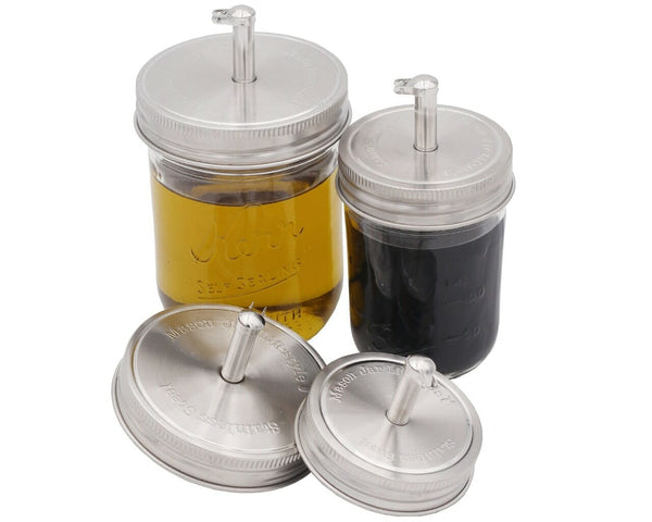 Two jars with silver lids and straws, one containing a yellow liquid and the other a dark liquid, on a white background.