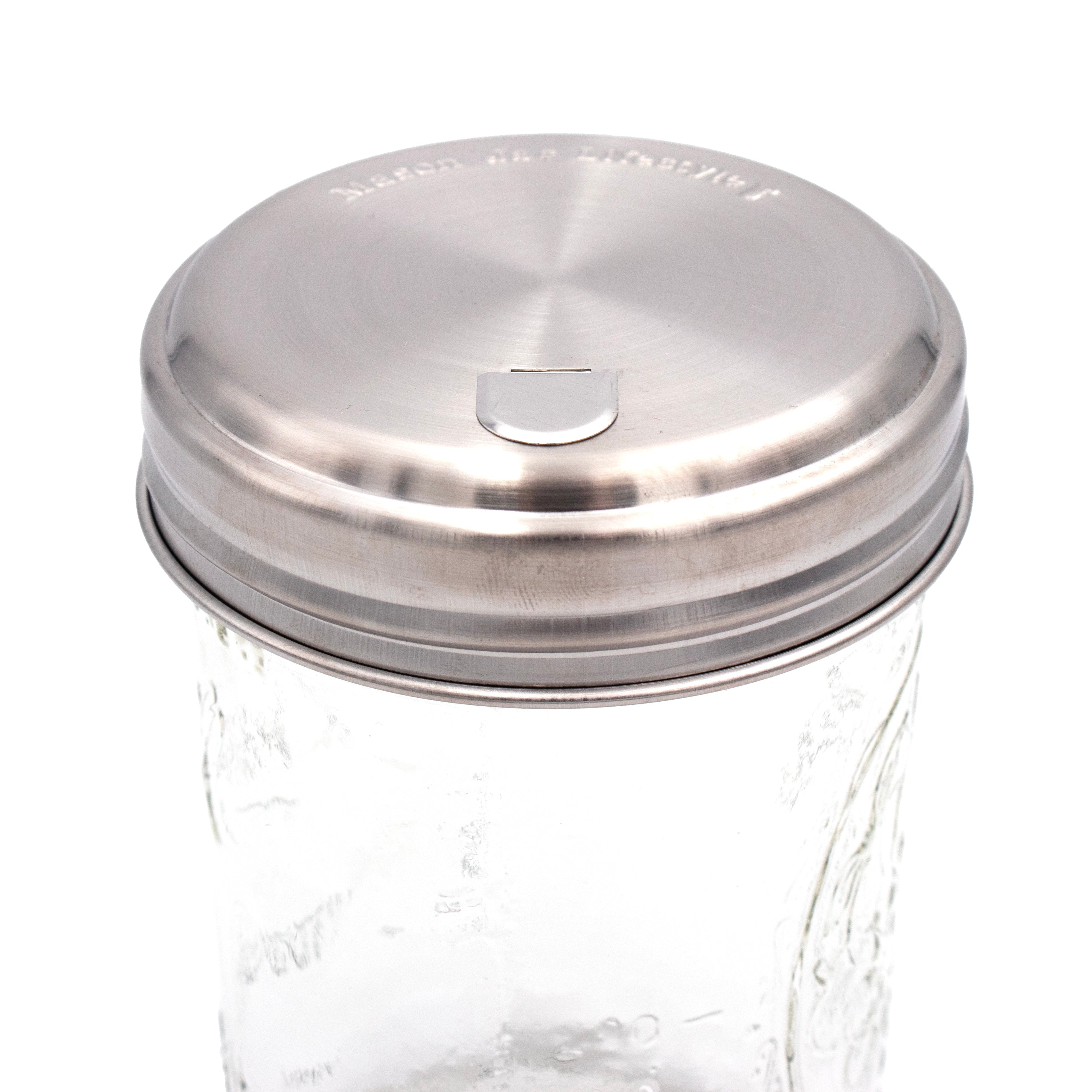 Glass jar with a silver metal lid on a white background. Transform your Mason jars with the Sugar Dispensing Stainless Steel Lids at Clozist. Rust-resistant, food-safe, and dishwasher safe. A durable 2-pack designed for easy pouring and sustainable kitchen organization. The perfect green gift for bakers and coffee lovers!