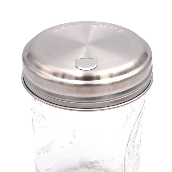 Glass jar with a silver metal lid on a white background. Transform your Mason jars with the Sugar Dispensing Stainless Steel Lids at Clozist. Rust-resistant, food-safe, and dishwasher safe. A durable 2-pack designed for easy pouring and sustainable kitchen organization. The perfect green gift for bakers and coffee lovers!